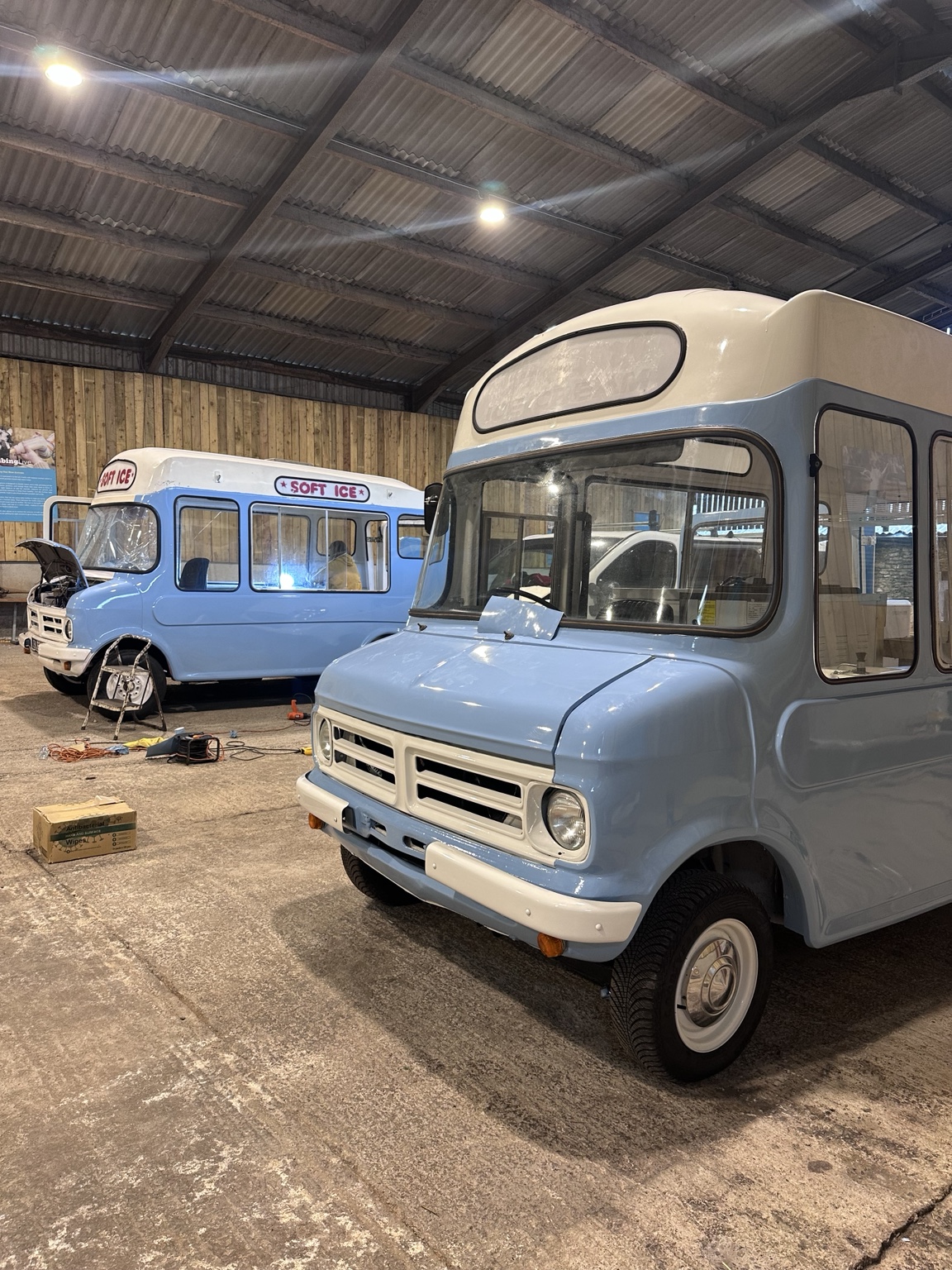 Two restored blue and white Bedford CF vans together in a workshop